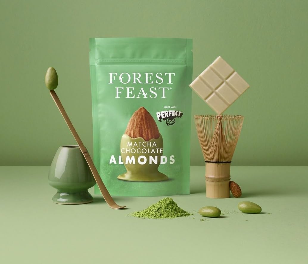 Forest Feast Matcha Chocolate Almonds in a mint green stand-up pouch, styled with a bamboo whisk, matcha powder, green chocolate covered almonds, and a white chocolate bar on a matching sage green background.
