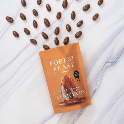 Packaging of Forest Feast salted caramel mini chocolate almonds on a marble surface with scattered almonds.