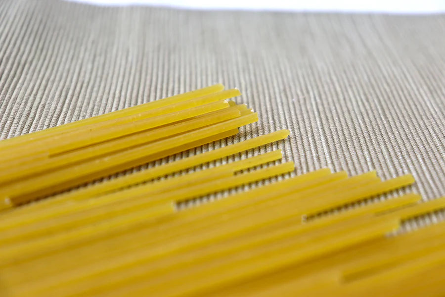 Uncooked spaghetti noodles arranged diagonally on a textured beige woven mat.