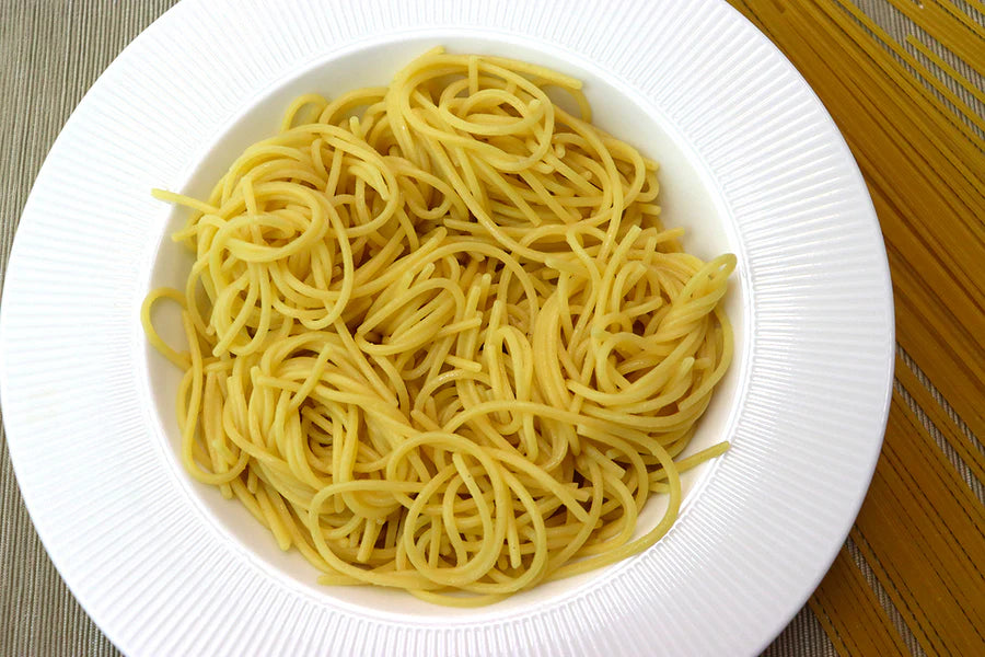 A top-down view of cooked spaghetti noodles in a white ribbed bowl, with a wooden surface visible on the right side.