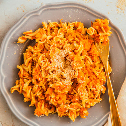 A top-down view of a bowl of orange pasta with a sprinkle of seasoning using Mill & Folks - Gluten Free pasta
