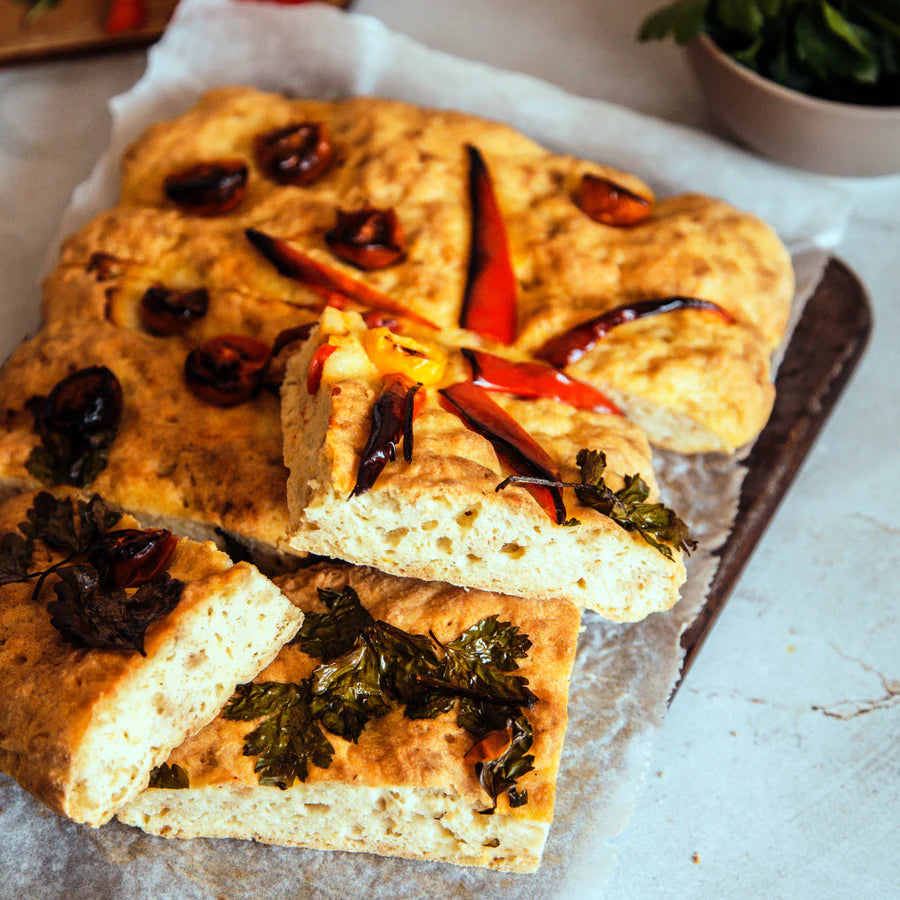 Freshly baked focaccia bread with embedded dried chili peppers and herbs, sliced and presented on parchment paper over a baking tray cooked using Bake-Free Low Carb Golden Bread flour mixture