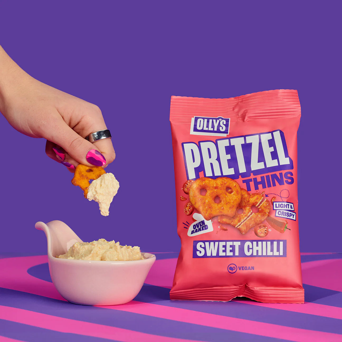 Olly's Sweet Chilli Pretzel Thins packaging with a hand holding a pretzel thins and a bowl with a dipping sauce.